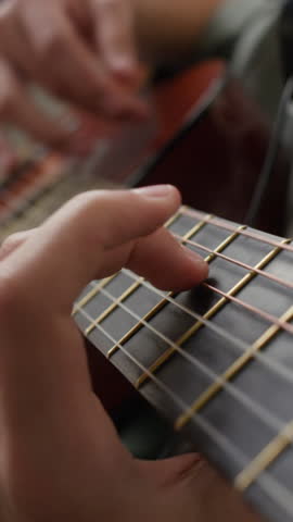 Vertical close-up view of hands of anonymous teenage musician playing acoustic guitar with wooden body and slapping it