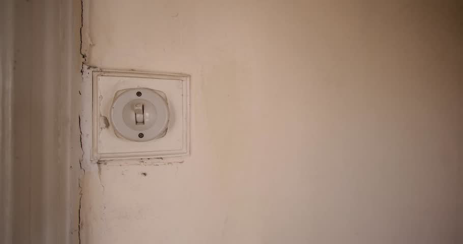 An old fashioned 1940's British house light switch made out of plastic showing a mans hand turning on and off again the electrical vintage switch in an old bedroom or living room.