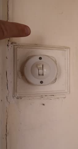 Portrait vertical footage of a man turning on and off an old Victorian British light switch in an old living room