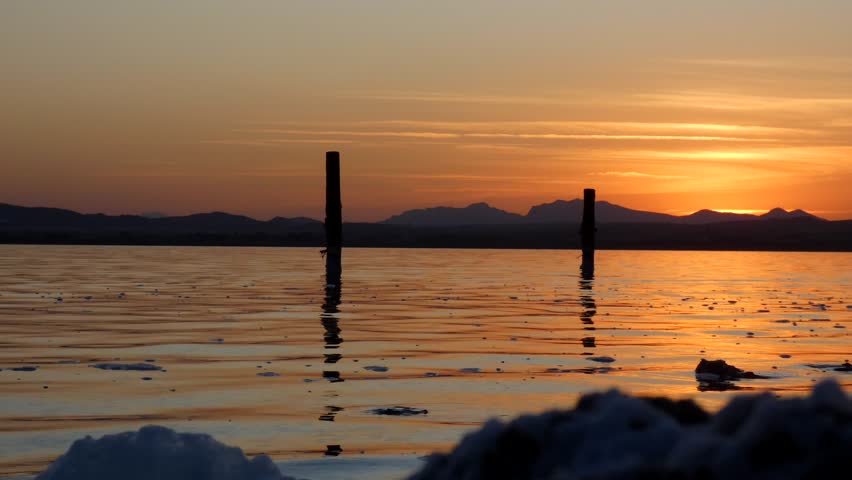 beautiful golden sunset above the calm lake with foam and behind the mountains