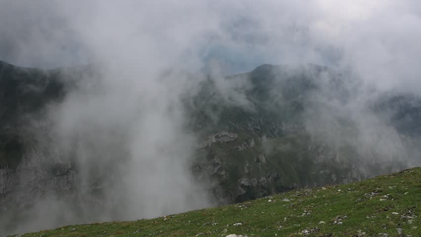 Impressive aerial view from above, down a spectacular valley, through very speedy moving clouds, forming the ceiling of a storm. The moving clouds are very close
