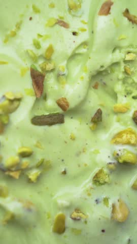 A vertical close-up showcasing gourmet pistachio ice cream with a topping of raw green nuts, emphasizing freshness and indulgence.