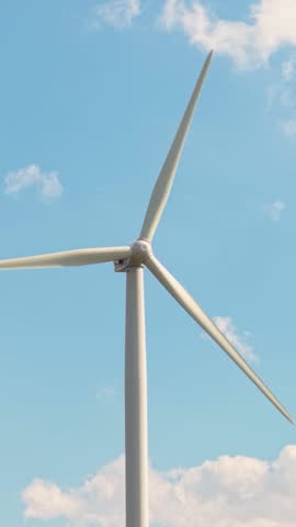 Wind turbine captured spinning under a sky full of white puffy clouds. A vertical composition symbolizing clean energy.