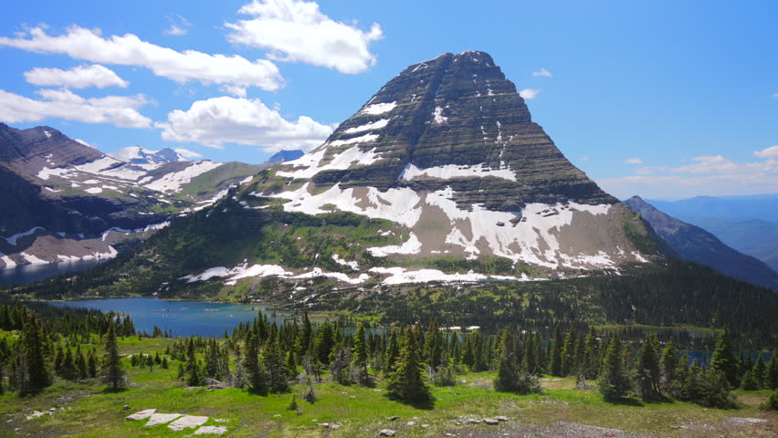 Experience the breathtaking landscapes of Glacier National Park in Montana, featuring majestic mountains, lush greenery, sparkling lakes, and clear blue skies filled with sunshine