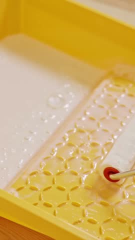 Vertical static shot shows a paint roller being saturated with primer inside a yellow tray, part of the hardwood floor preparation process to ensure better adhesion and smoother varnish application.