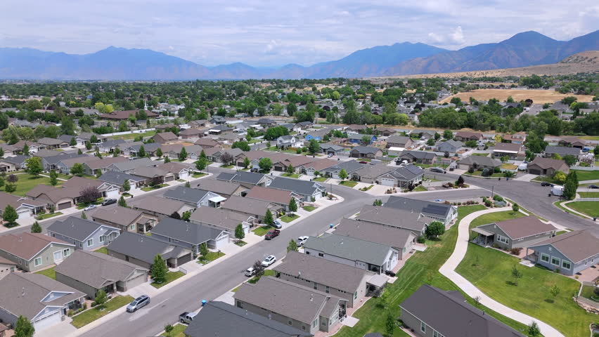 Explore a breathtaking aerial view of a picturesque Salt Lake City suburban neighborhood that is beautifully surrounded by stunning mountains, lush greenery, and abundant natural scenery