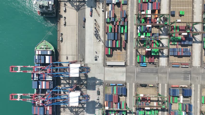 Vertical top down view of cargo containers piled on the quayside and cranes unloading goods from the ships, which are parking at the dock of Taipei Harbor, in Bali District, New Taipei City, Taiwan