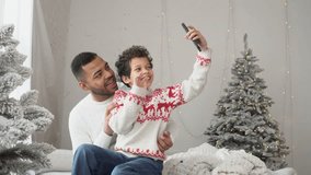 African American father and son talking on video call and wishing Happy New Year online near Christmas tree, man and teenager celebrating Christmas together at home and taking selfies on smartphone - Powered by Shutterstock - Get 15% off with code: PIKWIZARD15