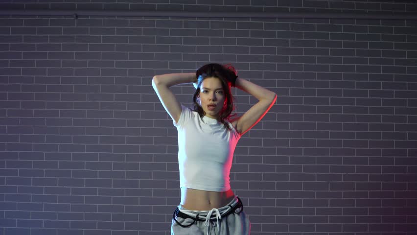 young crazy girl dancing hip hop against wall background in neon lighting, female choreographer moving to music and performing jazz funk in dance studio