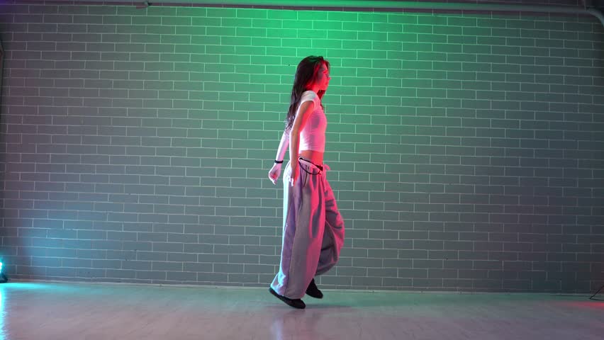 young crazy girl dancing hip hop against wall background in neon lighting, female choreographer moving to music and performing jazz funk in dance studio