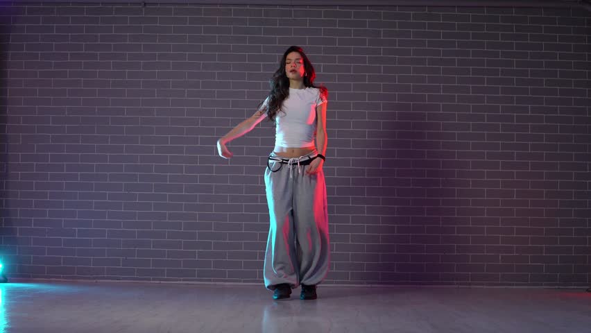 young crazy girl dancing hip hop against wall background in neon lighting, female choreographer moving to music and performing jazz funk in dance studio