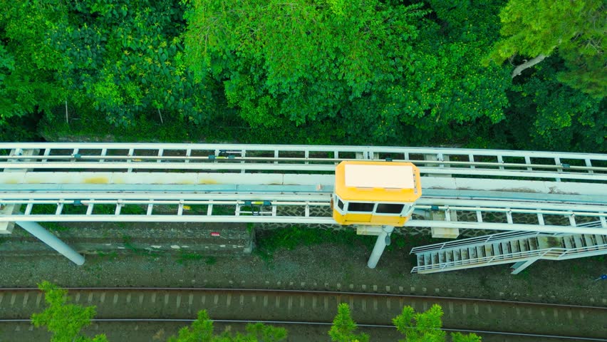 Aerial view of a yellow sky capsule moving on its track through green forest, alongside the coast and sea at Haeundae Blueline Park, Busan, Korea.