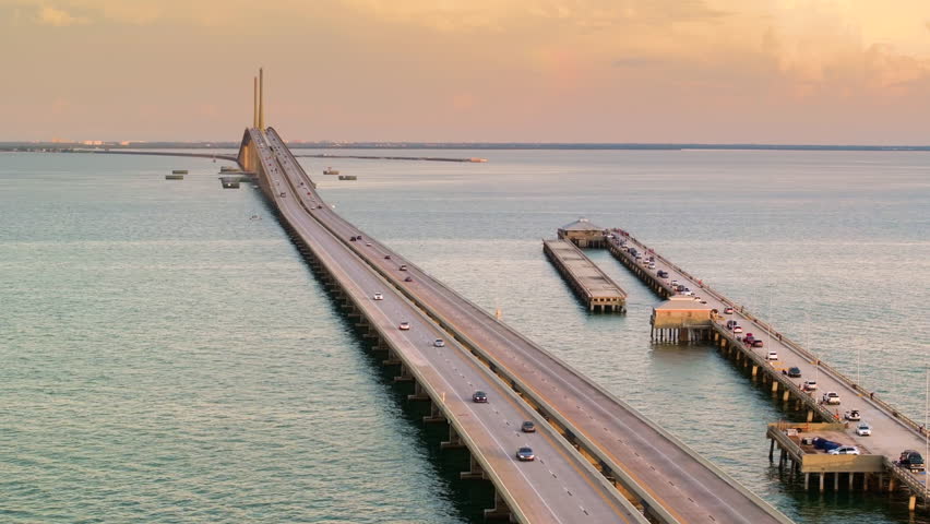 Sunshine Skyway Bridge over Tampa Bay in St Petersburg in Florida with fishing pier and driving traffic cars at sunset. Transportation infrastructure in USA.