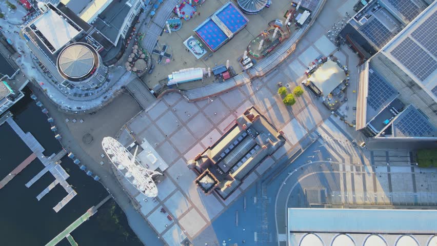 Aerial top down shot of a fair and large ferris wheel in Cardiff Bay, also features the Pierhead Building and people walking and rides in motion, 4K, 60fps