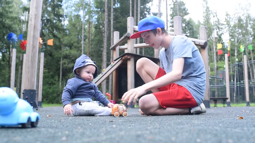 baby boy and his teenage brother playing on playground with toys in summer in park. children 12 years and 7 months
