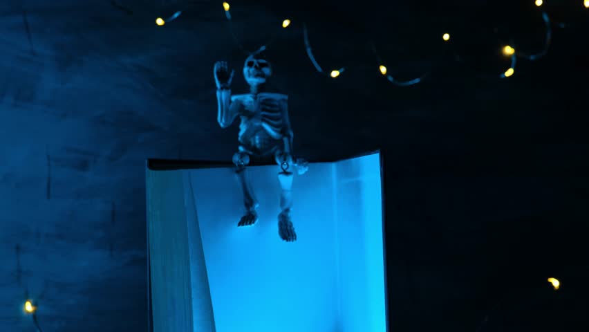 Halloween Stories. Skeleton in flickering light sits on book in dark. Halloween book mockup.Skeleton Puppet Reading Book at Night on chalkboard with blue light. 4k footage