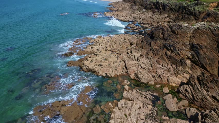 Drone flying over rocky coast and sandy Plage des Blancs Sablons, Le Conquet, Brittany, France. Aerial drone forward tilt-up reveal