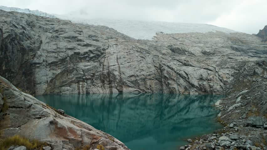 A spectacular aerial parallax shot orbits the majestic landscape of Paso del Zorro in the Peruvian Andes, revealing a vast glacier and a pristine, high-altitude alpine lake.