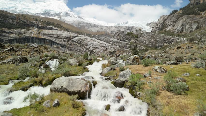 A thrilling, low-altitude drone shot flies rapidly over the rushing, whitewater stream that flows from the glacial waters of Laguna 513 in the high Andes of Peru.