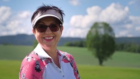 Confident senior woman golfer hitting with a golf club and smiling at the camera on a golf course, enjoying active retirement, healthy outdoor lifestyle, and leisure time on a bright summer day. - Powered by Shutterstock - Get 15% off with code: PIKWIZARD15