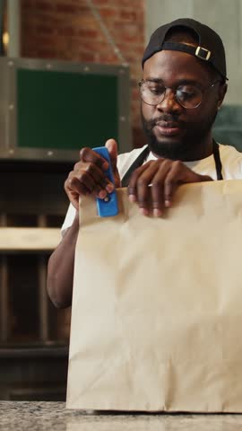 A dedicated worker folds a brown paper bag, preparing it for an order in a quaint cafe, surrounded by rustic decor and warm ambiance