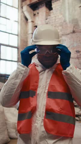 A worker puts on safety gear including gloves and a helmet in a bustling industrial location. Focused on ensuring secure conditions during the job