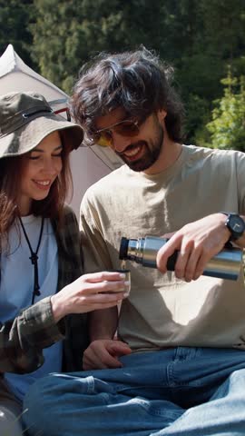 A couple sharing a joyful moment as they pour warm drinks, surrounded by beautiful nature, radiating warmth and connection on a bright afternoon