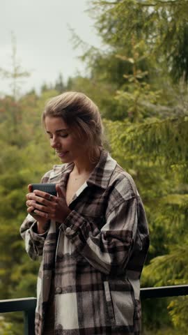 A young woman savors a peaceful morning in the woods, wrapped in a warm flannel shirt while enjoying her drink and soaking in the tranquility of nature