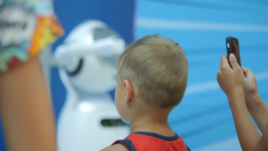 Robot with glasses is standing in front of another robot. The robot with glasses is wearing a pair of sunglasses