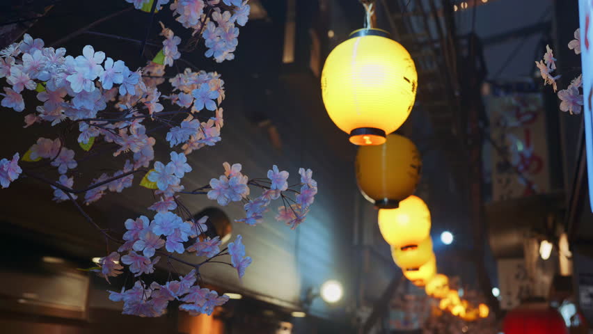 Lighted paper lanterns hanging with cherry blossom flower decorations on the on the Omoide Yokocho Memory Lane in the evening