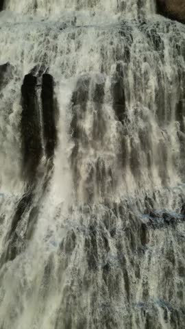 Aerial view of a powerful, multi-tiered waterfall cascading down dark, rocky terrain, creating a mesmerizing display of nature's force, Ísafjarðarbaer, Iceland.