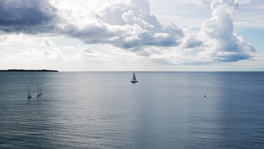 White sailboat sailing on calm ocean water with other boats in the distance, under a cloudy sky, Piran, Slovenia
