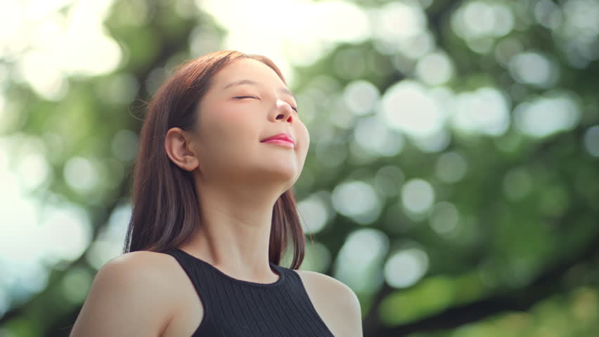 Peaceful asian woman practicing meditation and deep breathing in park for mindfulness and spiritual wellness, embracing fresh air and nature for healing energy balance with closed eyes and calm aura