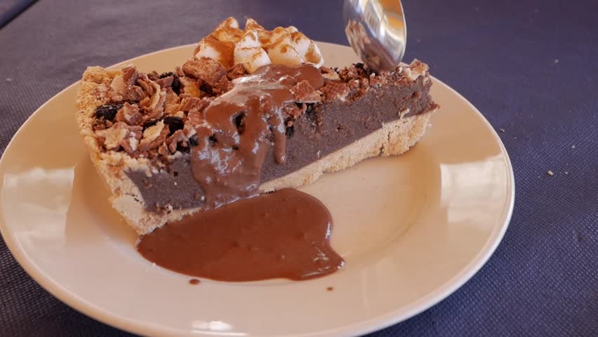 Static view of a tea spoon taking a piece of chocolate cheese cake with cream and chocolate sauce.