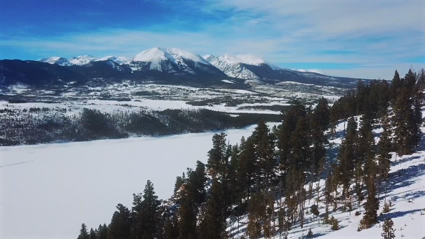 Aerial view of snow-covered mountains and a frozen lake, with a coniferous forest on a hillside, Dillon, Colorado, United States.