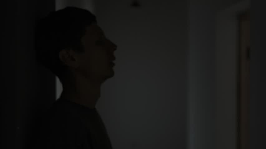 Silhouette of man alone in hallway hiding face with hands after breakup. A heavy feeling of loneliness