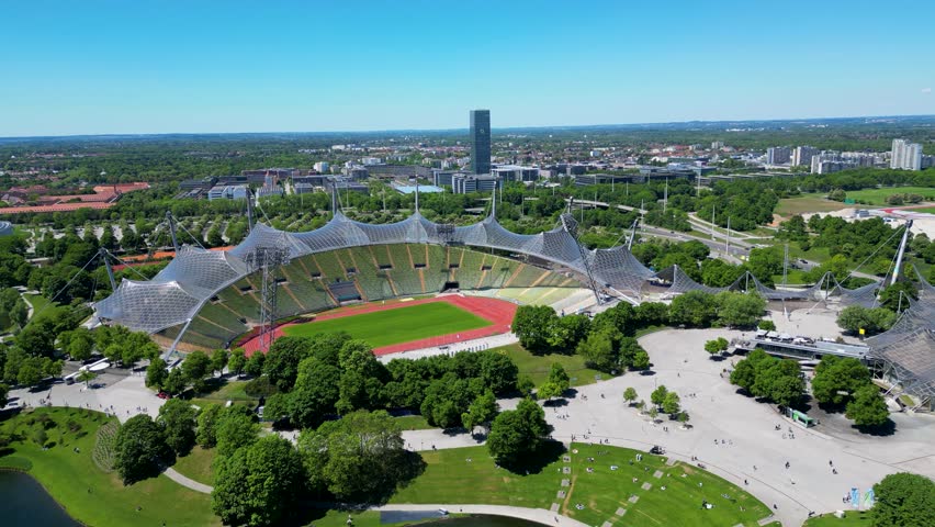 Aerial view of the Olympiastadion, a stadium with a distinctive translucent canopy surrounded by lush green trees and pathways, Munchen, Bayern, Germany.