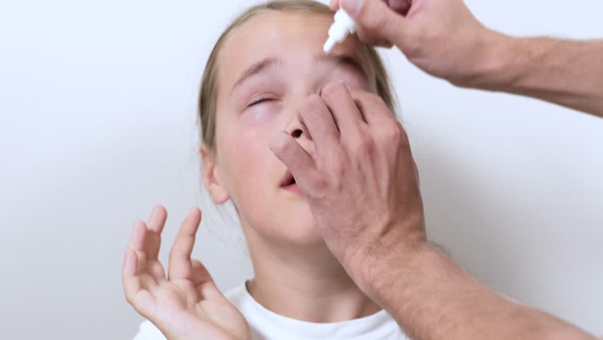 Child undergoing eye examination at ophthalmologist’s clinic. Doctor administering eye drops to dilate pupils for vision checkup. Pediatric eye care and medical health concept.