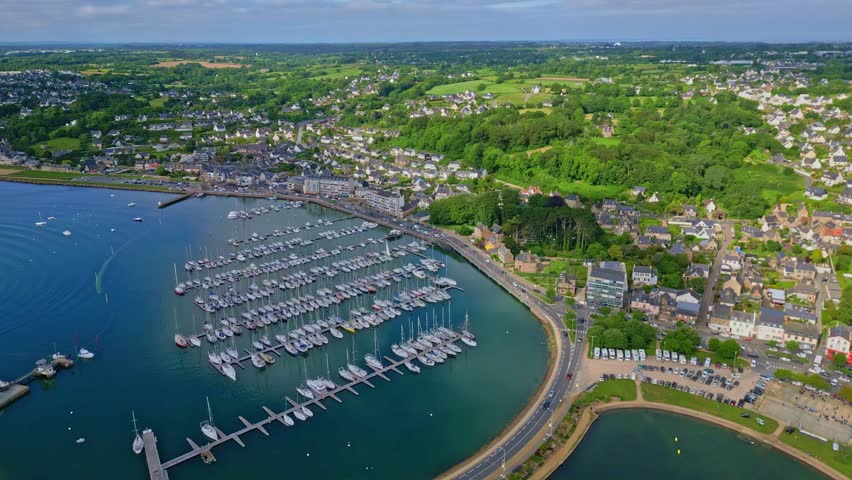 Perros-Guirec harbor with sailboats, coastal town, bridge, and green countryside, Brittany, France. Aerial drone backward
