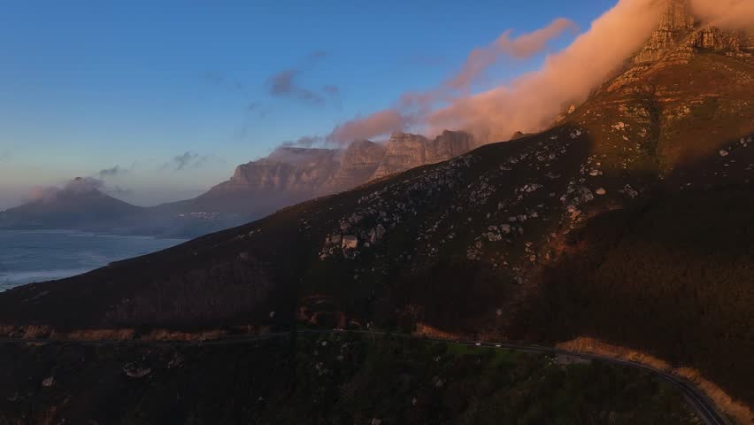 Aerial view of Table Mountain covered in clouds with the ocean in the background, bathed in the warm glow of sunrise, Cape Town, Western Cape, South Africa.
