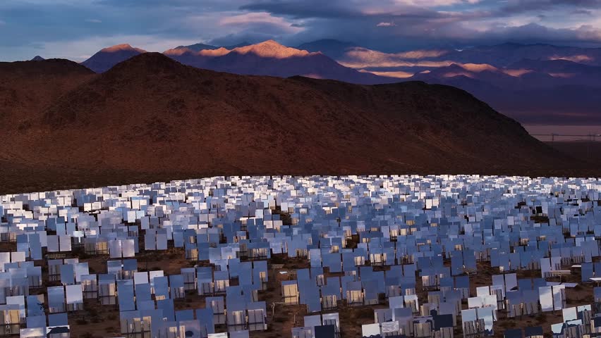 Aerial view of a large solar farm contrasting with the arid desert landscape, under a dramatic sky in San Bernardino County, California, United States.