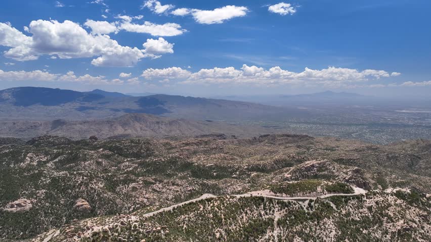 Aerial view of the rugged Santa Catalina Mountains, where a winding road cuts through the arid landscape under a bright, cloudy sky, Summerhaven, Arizona, United States.