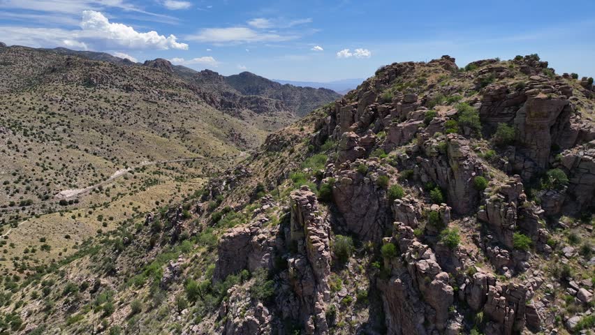 Aerial view of the rugged Santa Catalina Mountains, showcasing a tapestry of brown rocks and sparse green vegetation under a vast blue sky, Santa Catalina Mountains, Arizona, United States.