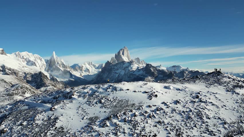 Drone shot of hikers on a sow covered summit in Patagonia, with the snow-covered peaks of Fitz Roy and Cerro Torre.