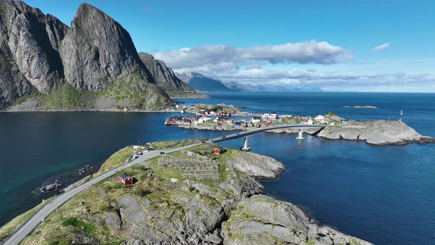 Aerial follows E10 to Hamnoy bridge with Festhaeltinden, fishing village, fjord and sea beyond