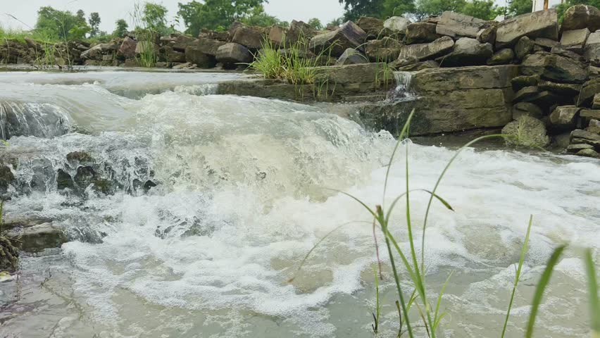 Closeup of a rocky cascade where water tumbles down over irregular rock formations amidst a lush, green environment, The dynamic flow of the water creates white foamy rapids, contrasting with the dark