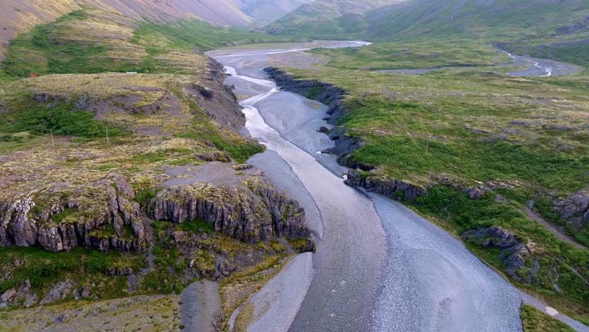 Aerial view of a glacial river winding through a valley with lush green vegetation, creating a striking contrast with the stark grey riverbed, Vik, Iceland.