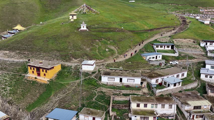 Aerial view of Serxu Monastery, where golden roofs contrast with white buildings amidst lush green hills, creating a serene, spiritual landscape, Serxu, Sichuan, China.