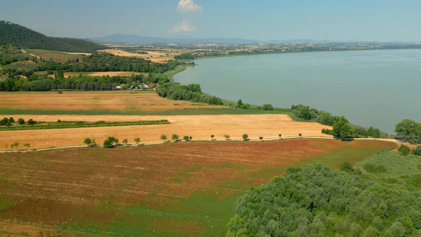 Aerial panorama revealing cultivated agricultural fields bordering scenic lake trasimeno, capturing verdant umbrian countryside landscape with expansive water and rural road