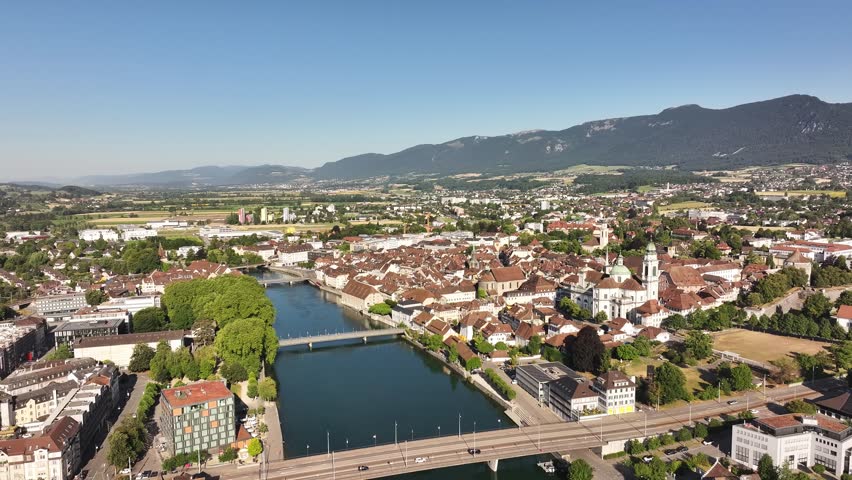 Aerial view of the city of Olten, Switzerland, with the Aare River flowing through its center. The historic cityscape is framed by green hills under a bright, the Swiss canton of Solothurn.